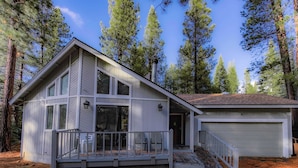 A two-story house with a covered porch, a garage, and a forested backdrop. - Oglala Little Lodge - Cabin Getaway (South Lake Tahoe)
