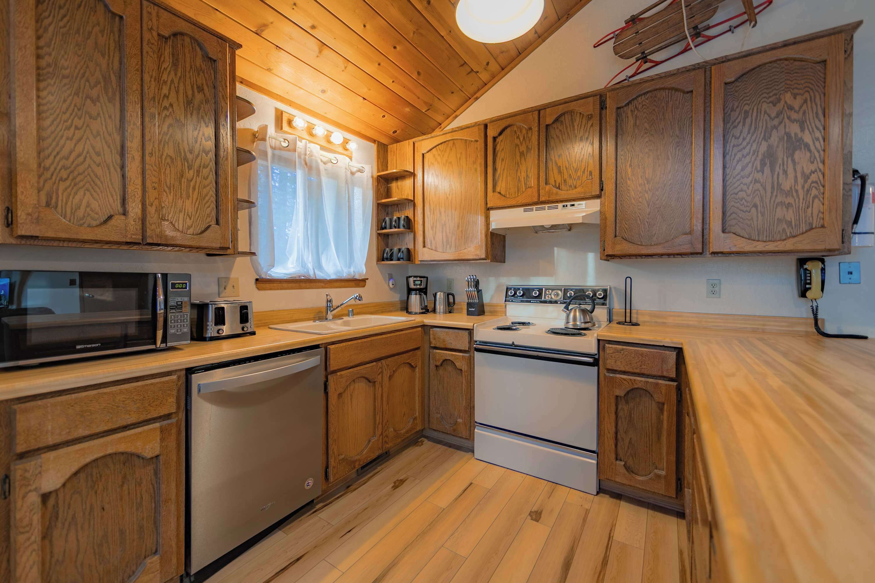 Una cocina con armarios de madera, microondas, tostadora, pileta y estufa.