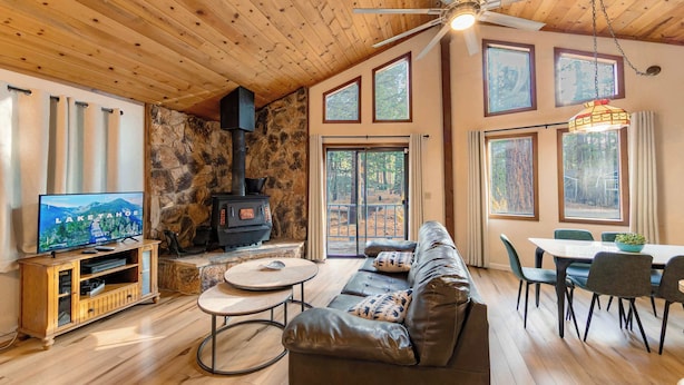 A cozy living room with a stone fireplace, wooden ceiling, and large windows. - Oglala Little Lodge - Cabin Getaway (South Lake Tahoe)