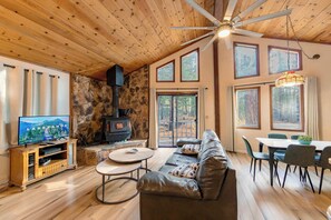 Ein gemütliches Wohnzimmer mit Kamin aus Stein, Holzboden und großen Fenstern.