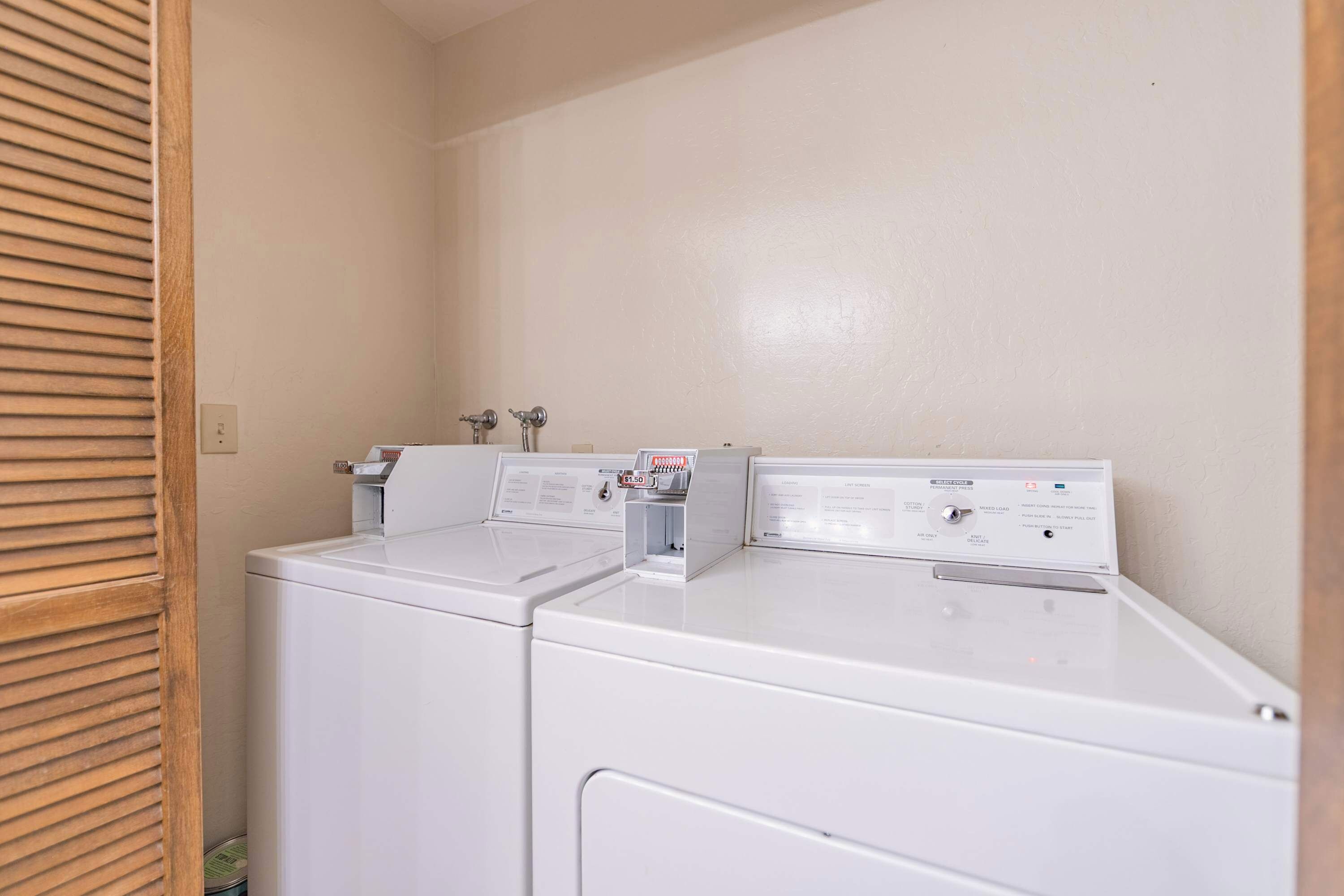 A laundry room with two white front-loading washing machines and a dryer, with a wooden slatted door on the left.