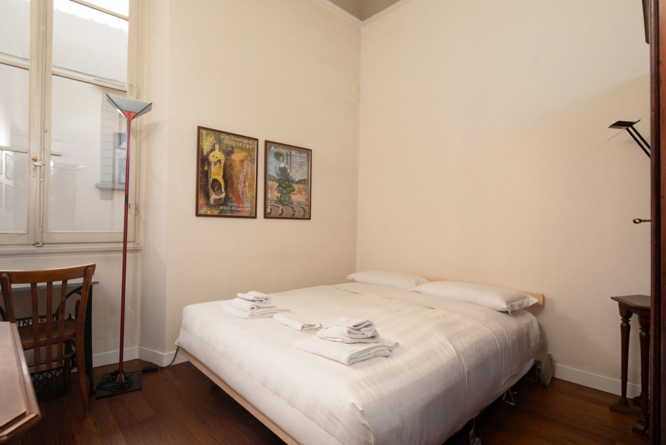 Een slaapkamer met een bed, een stoel, een tafel en twee posters aan de muur.