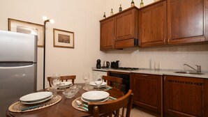 A kitchen with wooden cabinets, a refrigerator, a dining table set with plates and glasses, and a coffee maker. - Frescoed Duomo Retreat (Firenze)