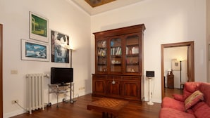 A living room with a wooden cabinet, a television, and a red sofa. - Frescoed Duomo Retreat (Firenze)