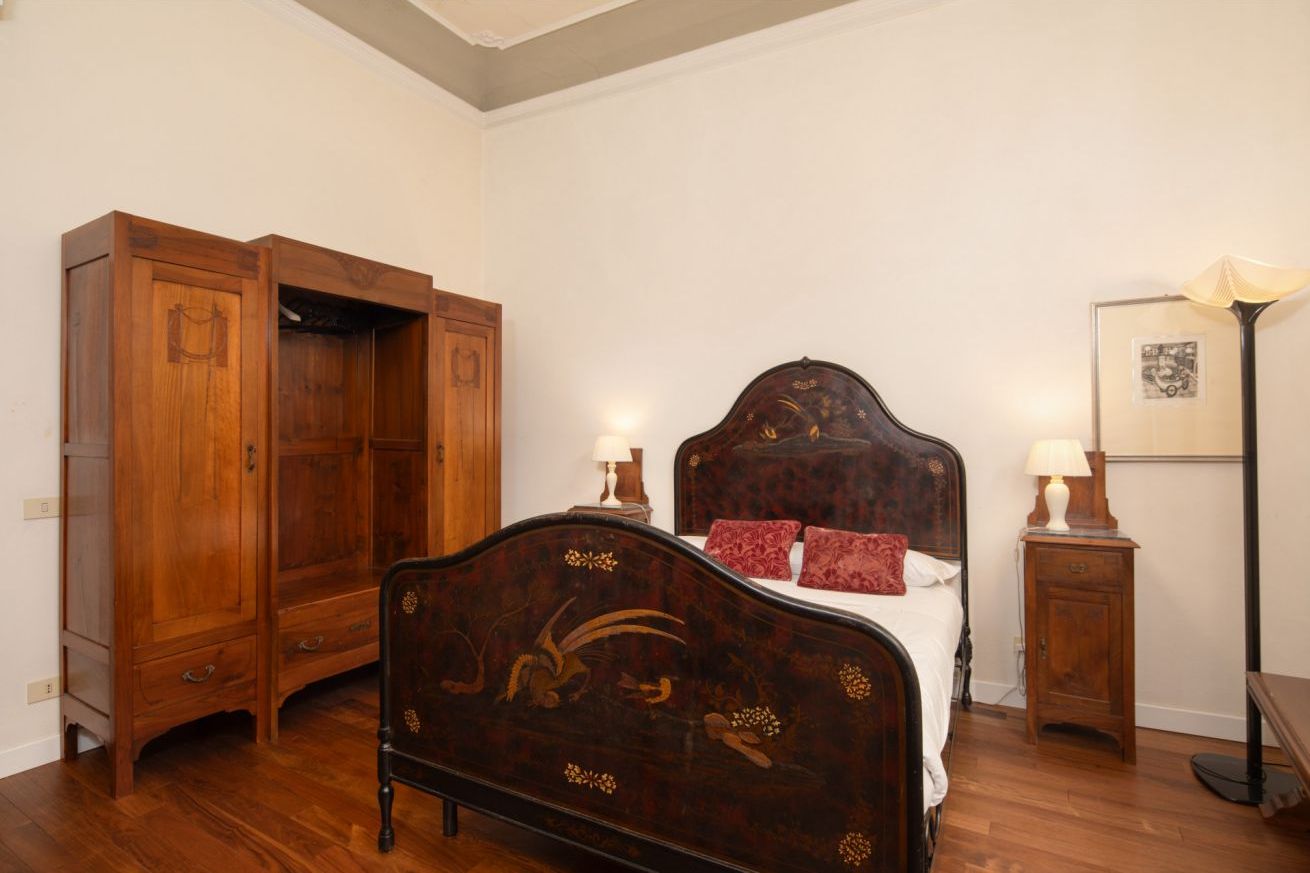 A bedroom with a wooden bed, a wardrobe, and a nightstand with a lamp.