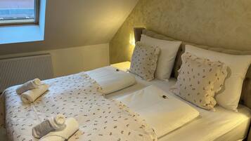 Una cama bien hecha con ropa de cama floral y toallas enrolladas, un radiador y una ventana con vistas.