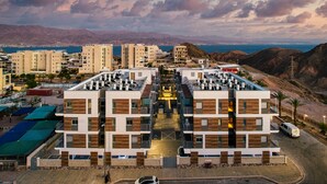 A modern building with multiple floors, a central courtyard, and a view of the sea and mountains in the background. - Modern Eilat Escape by Sea N' Rent (Eilat)