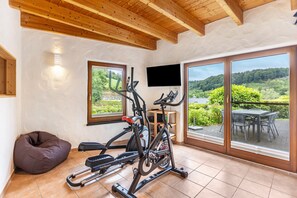 A gym with exercise equipment, a television, and large windows with a view of greenery.