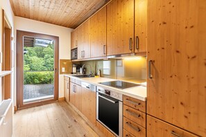 A modern kitchen with wooden cabinets, stainless steel appliances, and a large window offering a view of greenery.