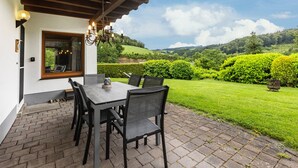 Eine Terrasse im Freien mit Tisch und Stühlen, einer Holzbeschichtung und Blick auf eine grüne Landschaft.