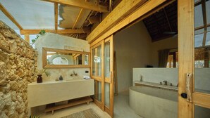 A modern bathroom with a stone wall, wooden beams, a large mirror, and a bathtub. - 7 BEDROOM BUNGALOW WITH POOL & A/C, NEAR MACAO BEACH (Punta Cana)