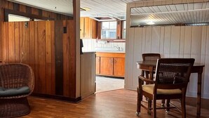 Um quarto espaçoso com piso de madeira, área de jantar com mesa e cadeiras, e cozinha com armários de madeira e uma janela.