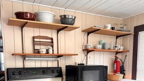 Uma cozinha compacta com fogão, micro-ondas e prateleiras de madeira com diversos utensílios de cozinha.