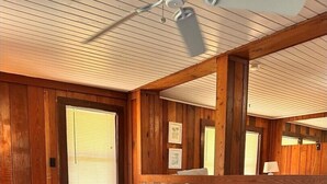Quarto com duas camas, paredes de madeira, ventilador de teto e janela com persianas.