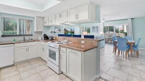 A modern kitchen with white cabinets, granite countertops, and a central island. - Ocean Villas Unit 118: Lagoon-Side Luxury with Direct Access (St. Augustine Beach)