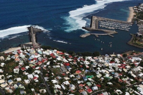 An aerial view of a coastal area with a densely packed residential neighborhood, a marina with boats, and a breakwater structure.