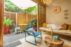 A cozy outdoor seating area with a wooden fence, a blue chair, a yellow table, and a wicker sofa with cushions.