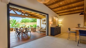 Un espacio habitable de concepto abierto con techo de madera, un comedor con mesa y sillas, una cocina con mostrador y alacenas, y vistas al exterior.