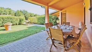 Un patio exterior con una mesa y sillas, rodeado de un jardín y una vista despejada del cielo.