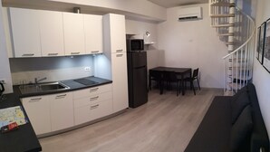 Eine kleine Küche mit weißen Schränken, einem schwarzen Kühlschrank und einem Essbereich mit Tisch und Stühlen.