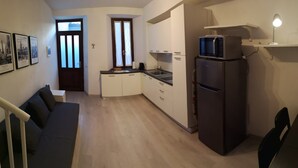 Eine kleine Küche mit Kühlschrank, Mikrowelle und Spüle. Ein Sofa und ein Esstisch mit Stühlen sind ebenfalls vorhanden.