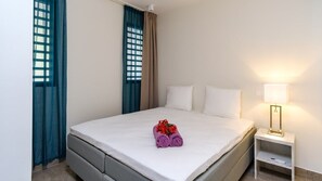 A hotel room with a bed, a nightstand, a lamp, and a window with curtains. - Stylish sea-view apartment with sunset terrace (Sint Willibrordus)
