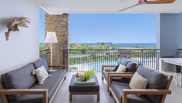 A balcony with a stone wall, two sofas, a coffee table, and a view of the ocean. - Stylish sea-view apartment with sunset terrace - Coral Estate (Sint Willibrordus)
