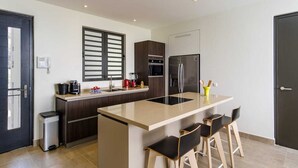 A modern kitchen with a central island, bar stools, a refrigerator, oven, and a coffee maker. - Stylish sea-view apartment with sunset terrace - Coral Estate (Sint Willibrordus)