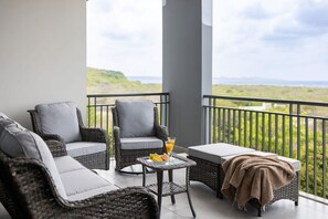 En balkon med fletmøbler, et glasbord med en drink og udsigt over landskabet.