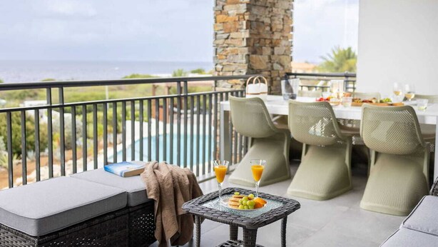 A balcony with a stone pillar, outdoor seating, and a table set for breakfast. - Luxury sea-view apartment with terrace - Coral Estate (Sint Willibrordus)