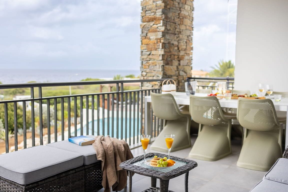 A balcony with a stone pillar, outdoor seating, and a table set for breakfast.