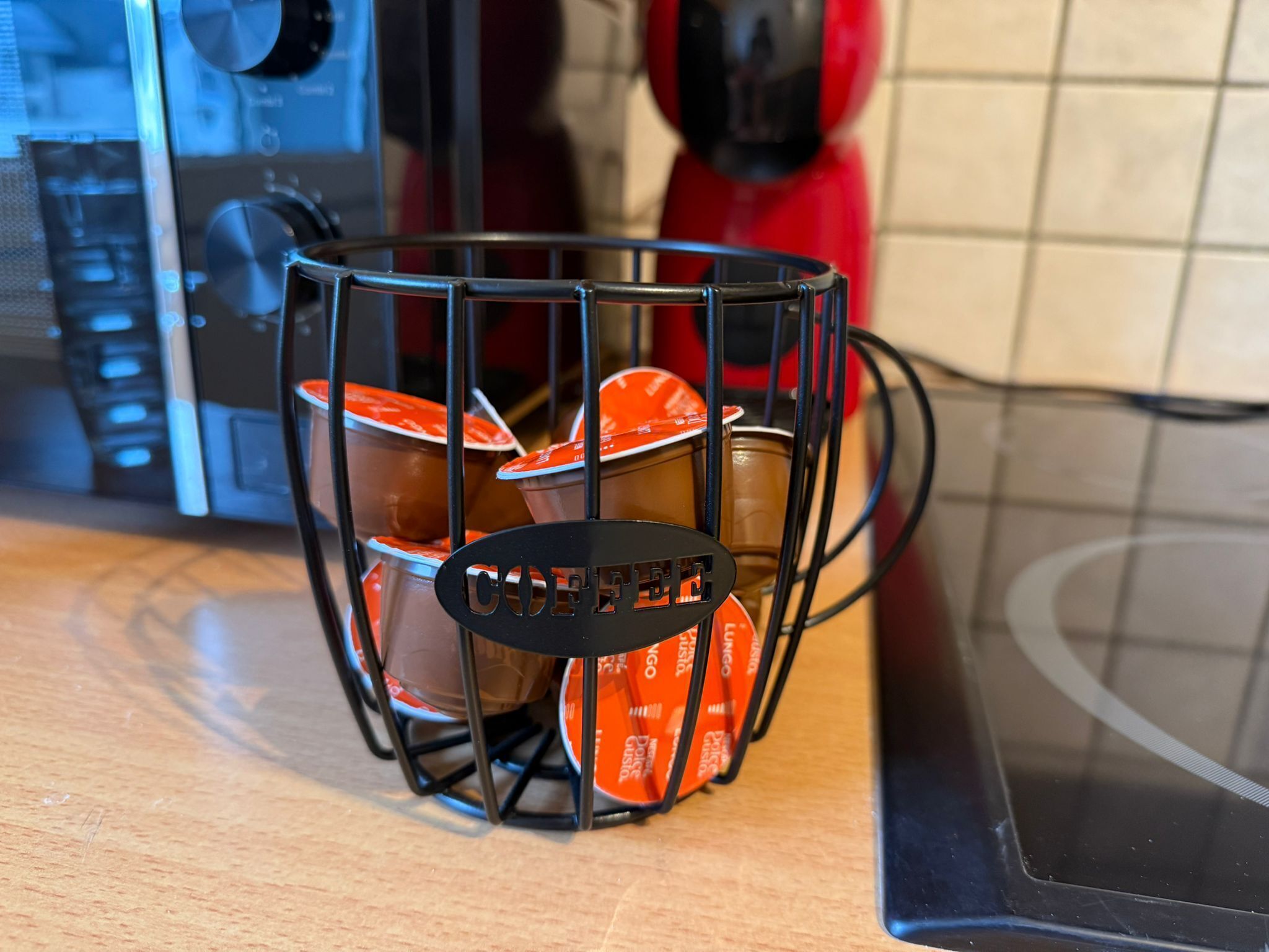 A kitchen counter with a coffee maker and a metal basket containing several orange cups.
