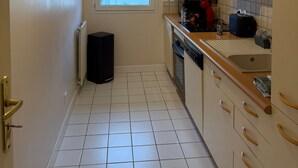 Pieni, käytännöllinen keittiö, jossa on valkoiset kaapit, ikkuna ja patteri.
