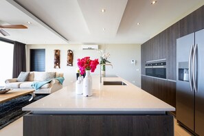 A modern kitchen with a central island, stainless steel appliances, and a dining area with a sofa and coffee table. - Luxury apartment with panoramic sea views (Sint Willibrordus)