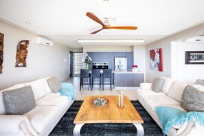 A modern living room with two white sofas, a wooden coffee table, and a ceiling fan. - Luxury apartment with panoramic sea views (Sint Willibrordus)