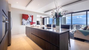 Una cocina moderna con una isla central, un amplio ventanal con vistas y una zona de comedor con sofá y mesa.