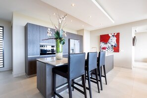 Eine moderne Küche mit grauen Schränken, einer zentralen Kochinsel mit Barhocker und einer großen Orchideenvase.