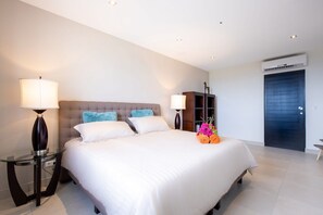 Ein modernes Hotelzimmer mit einem großen Bett, zwei Nachttischen mit Lampen, einem dunklen Holzschrank und einer Klimaanlage an der Wand.