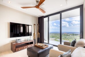 A modern living room with a flat-screen TV, wooden entertainment unit, and a large window offering a view of the ocean. - Luxury apartment with panoramic sea views (Sint Willibrordus)