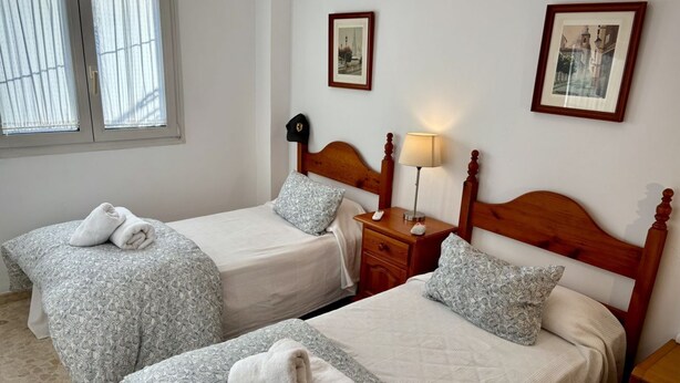 A hotel room with two beds, each with a wooden headboard, a bedside table with a lamp, and a window with blinds. - DescubreHome La Casa del Medico (Aznalcázar)
