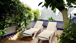 A patio with two white lounge chairs, a tiled floor, and a wall decorated with blue and white tiles and green plants. - DescubreHome La Casa del Medico (Aznalcázar)