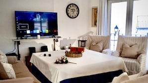 Een woonkamer met een televisie, een klok en een tafel met een mand en bloemen.