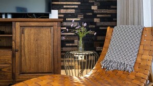 A wooden cabinet, a wicker chair with a patterned throw, and a vase with purple flowers against a wall with a geometric pattern. - Luxury ground-floor retreat with poolside terrace - Coral Estate (Sint Willibrordus)