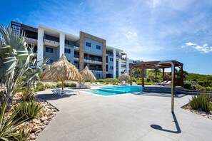 Un hotel moderno con piscina, asientos exteriores y una estructura de techo de paja.