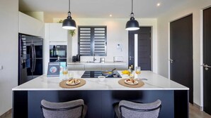 A modern kitchen with a central island, two pendant lights, and a dining area with two chairs. - Luxury ground-floor retreat with poolside terrace - Coral Estate (Sint Willibrordus)