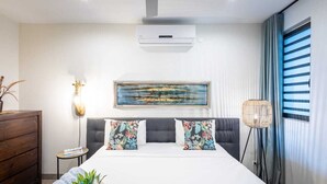 A modern bedroom with a large bed, a ceiling fan, an air conditioning unit, a framed painting, a side table, and a floor lamp. - Luxury ground-floor retreat with poolside terrace - Coral Estate (Sint Willibrordus)