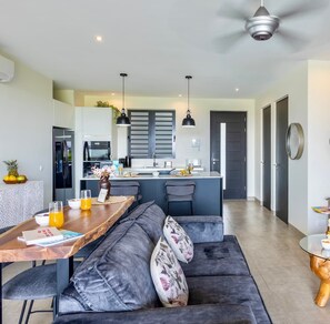 A modern kitchen with a central island, a dining area with a wooden table and black upholstered seating, and a ceiling fan. - Luxury ground-floor retreat with poolside terrace (Sint Willibrordus)