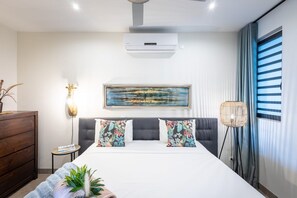 A modern bedroom with a large bed, a wall-mounted air conditioner, a framed painting, and a floor lamp. - Luxury ground-floor retreat with poolside terrace (Sint Willibrordus)