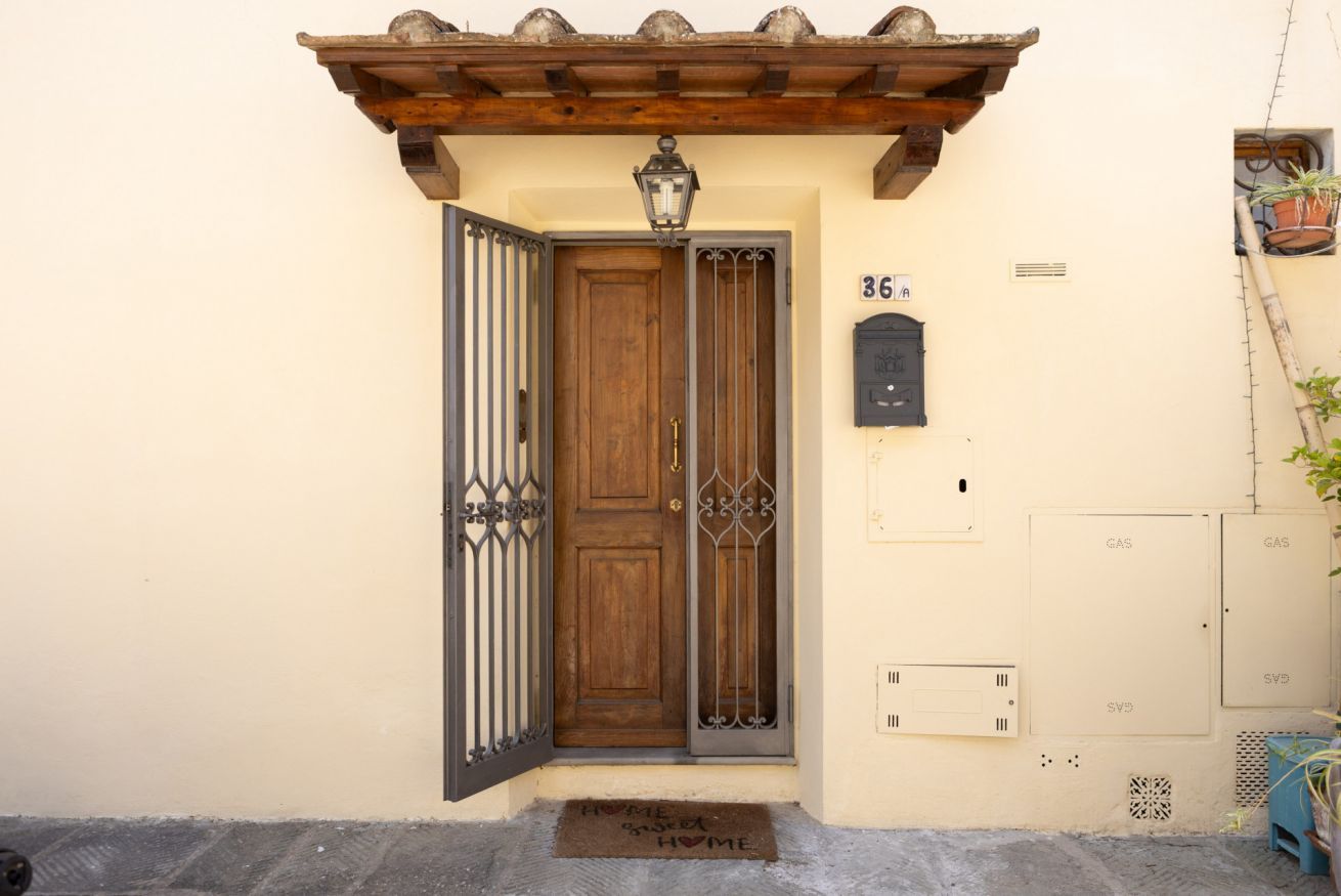 A wooden door with a metal gate, a mailbox, and utility boxes on a beige wall.