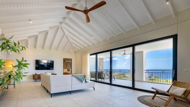 A spacious living room with a white sofa, a flat-screen TV, and a large sliding glass door leading to a balcony with a view of the ocean. - Luxury penthouse with panoramic sea views - Coral Estate (Sint Willibrordus)